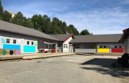 Slettaelva barnehage sett utenfra en solrik sommerdag med blå himmel og grønn skog